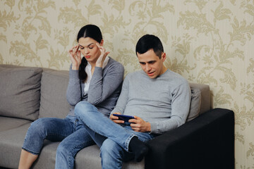 Gamer husband plays on smartphone, angry wife sits nearby