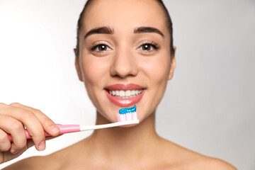 Woman holding toothbrush with paste on light background