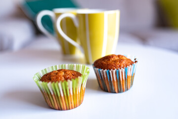 Muffins with colored wrappers and green cups on top of a white table