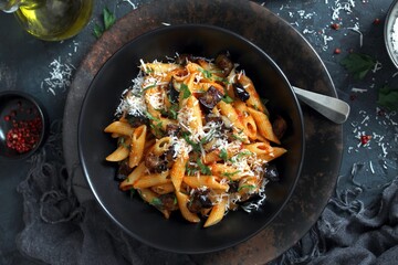 Pasta alla norma - Italian pasta with eggplant, tomato and parmesan cheese on dark table. Top view with copy space.