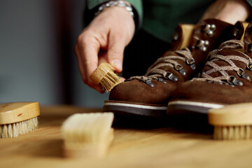 Man's hand clean suede shoes, boots with a brush on wooden background.