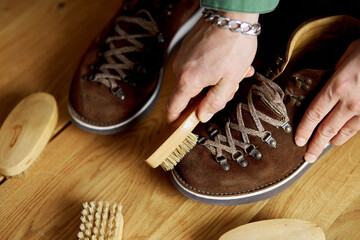 Man's hand clean suede shoes, boots with a brush on wooden background.