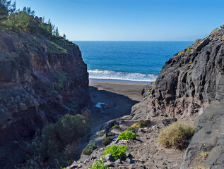 Fototapeta na wymiar Mouth of Barranco de Guigui Grande gorge with view of empty sand beach Playa de Guigui in west part of the Gran Canaria island, accessible only on foot or by boat. Canary Islands, Spain
