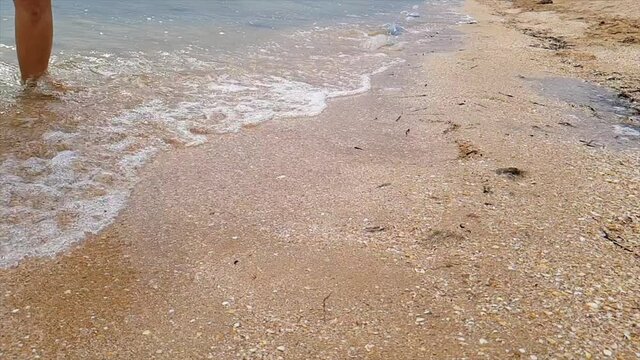 The wave washes away the heart nestled in the sand. Woman draws a heart in the sand. A woman draws a heart on the seashore which is washed away by a wave.