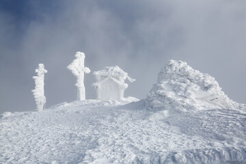 Landscape of high mountains. Snow coted building and cross on a snow covered lawn. Fog on the...