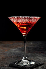 Red alcoholic cocktail with tequila, strawberry syrup and crushed ice, in a cocktail glass on a black background