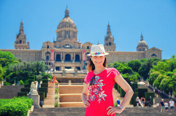 Barcelona, Spain, June 12, 2017: Young woman traveler with red dress and hat looking at camera, smiling and posing in sunny summer day, National Palace Montjuic and National Art Museum of Catalonia