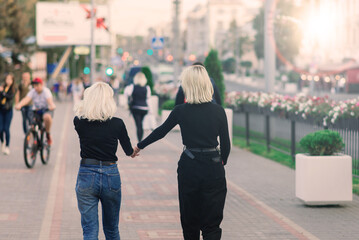 Two young females walking smiling embracing and kissing outdoor in the city
