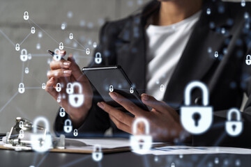 Businesswoman in formal wear signing the contract to prevent probability of risks in cyber security. Checking the phone. Padlock Hologram icons over the working desk.