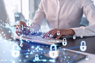 A woman programmer is typing a code on computer to protect a cyber security from hacker attacks and save clients confidential data. Padlock Hologram icons over the typing hands. Formal wear.