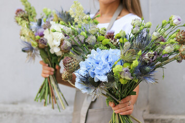 A young girl florist is holding two bouquets of drided and blue flowers in her hands