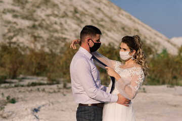 Young loving couple in medical masks in park during quarantine on wedding day.