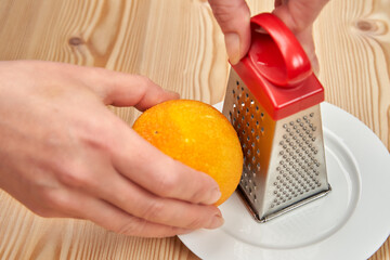 Rub the orange peel on a mini grater. Close-up.