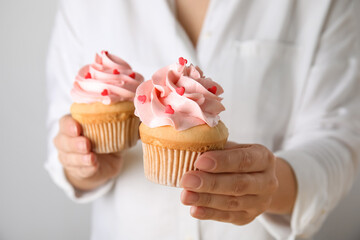 Fototapeta na wymiar Woman holding tasty cupcakes for Valentine's Day on light background, closeup