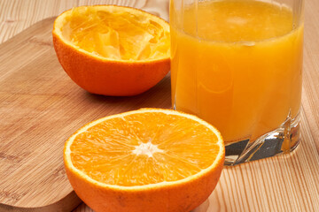 A glass of orange juice with cut oranges on a wooden table. Side view Close-up.