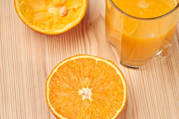 A glass of orange juice with cut oranges on a wooden table. Side view Close-up.