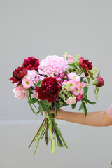 A bouquet of pink and Burgundy peonies in hand of a girl on a gray background