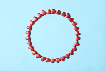 Round frame made of bright heart shaped sprinkles on light blue background, flat lay. Space for text