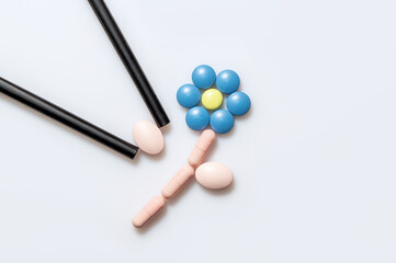 Fototapeta na wymiar Flower with leaves made from pills and chopsticks isolated on bright background. Blue tablet or pink painkiller as medical background. Pill for alleviating illness or fever 