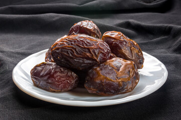 Big luxury dried date fruit in bowls on the dark surface, kurma ramadan kareem concept, close up.