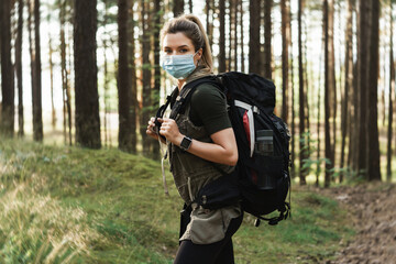 Woman hiker with a backpack wearing prevention mask during her hike in forest