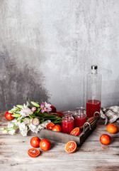 fresh blood orange juice in glasses and in bottle with fresh oranges in wooden tray on wooden table, copy space
