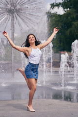 young woman in short skirt and white t-shirt having fun and laughing at the fountain in the city park. vertical