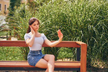 Young woman takes a selfie, sits on a bench in a city park.