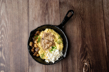 Banosh - a traditional dish in the Western Ukraine made of cornmeal. Served in a black pan with cracklings, mushrooms and hutsul cheese bryndza. Close-up on a wooden background with copy space.