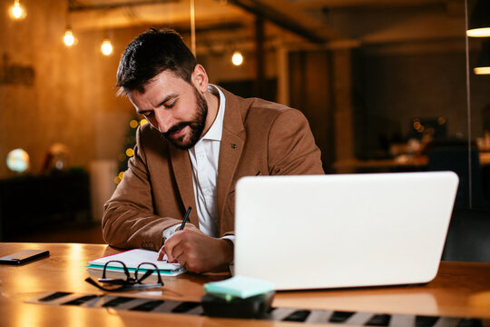 Young businessman using laptop in his office. Businessman taking a notes while working on laptop.