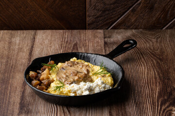 Banosh - a traditional dish in the Western Ukraine made of cornmeal. Served in a black pan with cracklings, mushrooms and hutsul cheese bryndza. Close-up isolated on a wooden background.