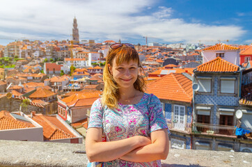 Young woman traveler with sunglasses on head with crossing arms, looking at camera and posing in front of Porto Oporto city historical centre with red tiled roofs in Portugal, backlit sun flare - obrazy, fototapety, plakaty