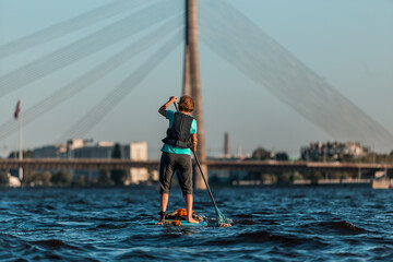 woman rowing with SUP stand up paddle boards along the river, in the background the cable-stayed bridge