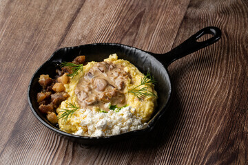 Banosh - a traditional dish in the Western Ukraine made of cornmeal. Served in a black pan with cracklings, mushrooms and hutsul cheese bryndza. Close-up isolated on a wooden background.