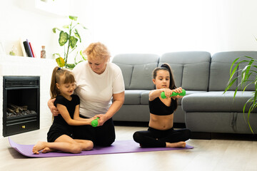 senior grandmother workout yoga withgranddaughters preschooler. They are sitting on mat at cozy home interior. Sport, parenthood and people concept - Powered by Adobe