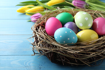 Fototapeta na wymiar Colorful eggs in nest and tulips on blue wooden background, closeup. Happy Easter