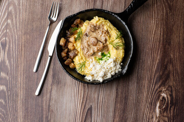 Banosh - a traditional dish in the Western Ukraine made of cornmeal. Served in a black pan with cracklings, mushrooms and hutsul cheese bryndza. Close-up on a wooden background with copy space.