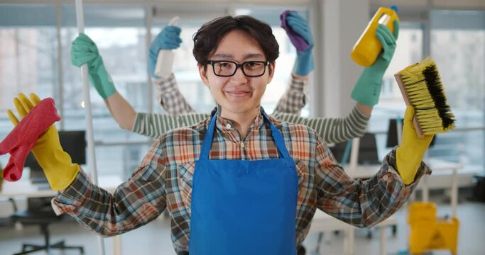 Portrait of asian multi-armed man janitor holding cleaning equipment and smiling at camera