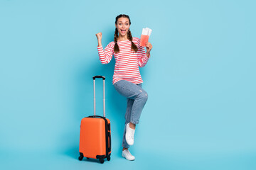 Full length photo of pretty lucky young woman dressed striped shirt holding luggage tickets isolated blue color background