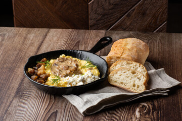 Banosh - ukrainian dish made of cornmeal. Served in black pan with cracklings, mushrooms and hutsul cheese. Close-up isolated on wooden background with sliced bread and grey linen napkin. Copy space.