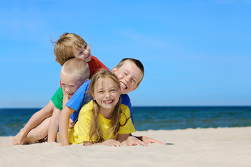 Fototapeta premium Two girls and two boys in colorful t-shirts playing on a sandy beach