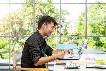 Young Asian businessman working at home with laptop in dining room, online meeting conference with colleague.