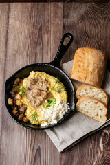 Banosh - ukrainian dish made of cornmeal. Served in black pan with cracklings, mushrooms and hutsul cheese. Close-up on wooden background with sliced bread and grey linen napkin. Top view, copy space.