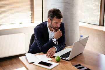 Naklejka premium Young businessman using laptop in his office. Businessman taking a notes while working on laptop
