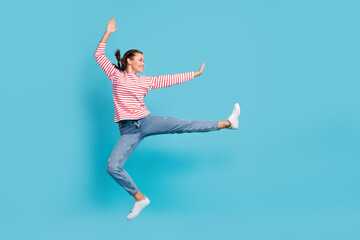 Full length photo of funny rejoicing young lady fighter wear red shirt jumping leg side isolated blue color background