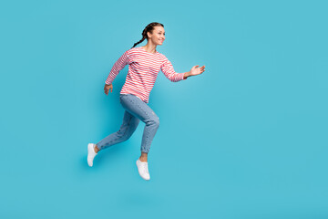 Fototapeta na wymiar Full length photo of pretty purposeful young woman dressed striped shirt jumping empty space isolated blue color background