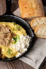 Banosh - a ukrainian dish made of cornmeal. Served in black pan with cracklings, mushrooms and hutsul cheese bryndza. Close-up isolated on a wooden background with sliced bread and grey linen napkin.