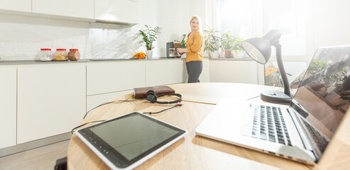 Young woman sitting in kitchen and working on laptop.