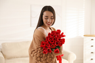 Happy woman with red tulip bouquet at home. 8th of March celebration