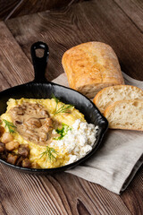 Banosh - a ukrainian dish made of cornmeal. Served in black pan with cracklings, mushrooms and hutsul cheese bryndza. Close-up isolated on a wooden background with sliced bread and grey linen napkin.